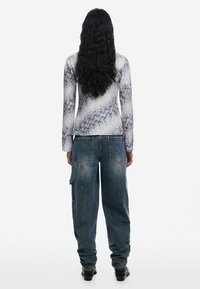 Tričko s dlhým rukávom má textúrovanú bielu tkaninu s modrými vlnovými vzormi; skombinované so voľnými modrými džínsovými nohavicami s vreckami.