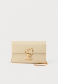Μπεζ δερμάτινη τσάντα με χρυσό κούμπωμα σε σχήμα καρδιάς. Διαθέτει λογότυπο στο μπροστινό μέρος και αλυσίδα-ιμάντα για ευελιξία.