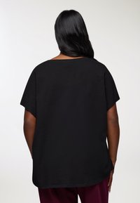 Czarna, krótko rękawowa koszulka z okrągłym dekoltem, charakteryzująca się luźnym krojem i gładką fakturą tkaniny. Prosta, jednolita kolorystyka bez wzorów.