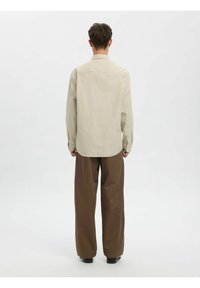 Langermet, lyst beige rutete skjorte med avslappet passform, knappemansjetter og avrundet hem, kombinert med brune vide bukser.