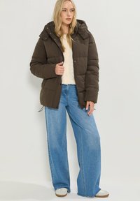 Brun pufferjacka med huva, med en kviltad design. Kombinerad med ljusblå vida jeans och beiga sneakers.