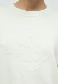 Λευκό βαμβακερό φούτερ με υφασμένο, κεντημένο λογότυπο σε επαναλαμβανόμενο μοτίβο στο κέντρο. Στρογγυλή λαιμόκοψη και ριμπ τελείωμα.