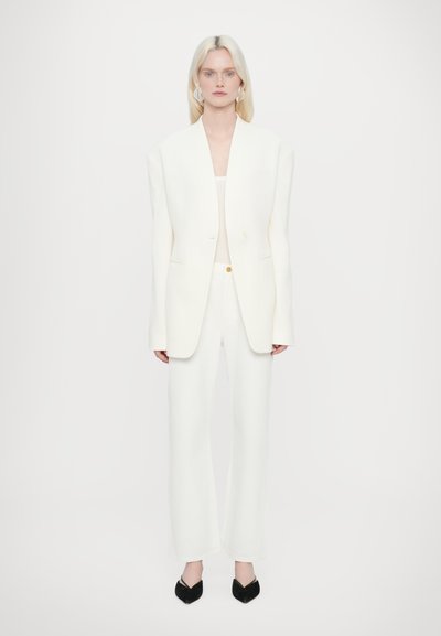 Witte oversized blazer met gestructureerde schouders, knoopdetails, gecombineerd met witte rechte broek en puntige zwarte schoenen.