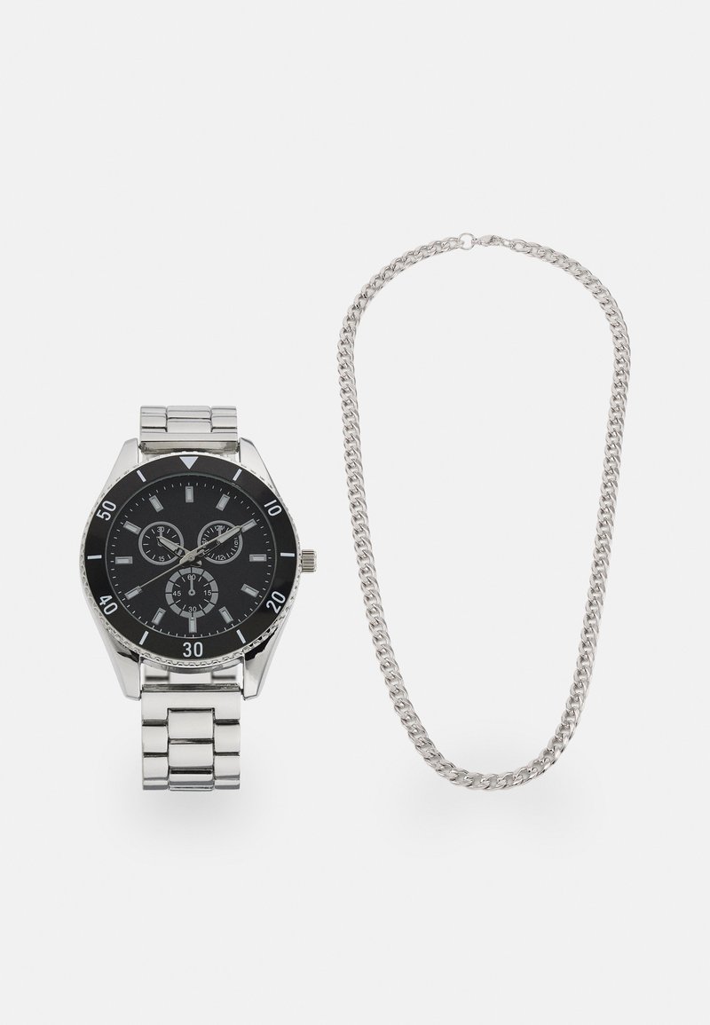 Sølv rustfrit stål ur med en sort urskive, tre subdials og link-armbånd. Følger med en sølv kæde halskæde.