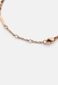 Rózsaarany lánc karkötő, homár csattal, összekapcsolódó láncszemekkel és márkanevet tartalmazó címkével. Simább textúra, fényes felülettel.