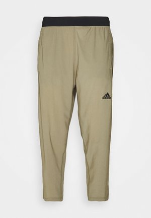 Beżowe spodnie dresowe Adidas z czarną elastyczną talią i bocznymi kieszeniami, z logo Adidas na prawej udzie.