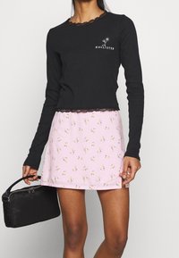 Zwarte longsleeve top met kantafwerking en een roze bloemenrok, versierd met kleine gele en groene patronen, gecombineerd met een zwarte clutch.