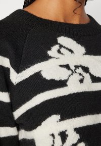 Maglione a maglia bianco e nero con scollo rotondo, caratterizzato da un audace design grafico e una texture morbida. Accentuato da strisce a contrasto.