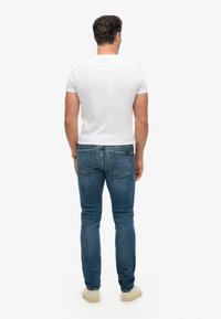 Camiseta blanca de manga corta combinada con jeans de mezclilla azul. La camiseta tiene un diseño simple; los jeans tienen bolsillos clásicos y un corte recto.