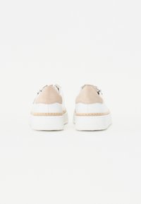 Baskets blanches avec des accents en daim beige, semelles plates et détail en corde tressée à la base, présentant un design à lacets et des ferrures métalliques.