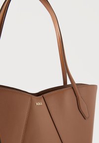 Καφέ δερμάτινη τσάντα ώμου με λεπτούς ιμάντες ώμου και μικρό χρυσό λογότυπο "BOSS" στη μέση του μπροστινού μέρους.