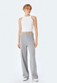 Hvid ribbet crop top parret med lysegrå vidde bukser med lodrette sømme og en blød tekstur. Modellen har sneakers på.