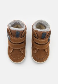 Braune Wildleder-Stiefeletten mit doppelten Klettverschlüssen, weißen Nähten und Kunstfellfutter am Kragen. Gummisohle für Traktion.