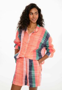 Linenová košeľa a šortky v koralovej farbe s vertikálnymi pruhmi zelenej, modrej a ružovej. Obsahuje tlačidlá, vrecká a vyhrnuté rukávy.