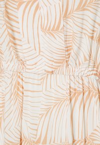 Tissu léger avec un fond crème orné d'un motif répétitif de feuilles de palmier douces et couleur pêche. Détail de taille froncée.