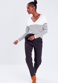 Pull à col en V rayé en blanc et noir avec des boutons sur l'épaule, associé à un pantalon noir ajusté et des bottines marron.