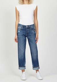 Ljusblå denimjeans med lös passform, urtvättad detaljering och uppvikta fållar. Kombinerat med en tajt vit t-shirt och vita sneakers.