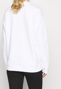 Vit sweatshirt med avslappnad passform, ribbade ärmar och nederkant, med en ren design. Tillverkad av mjukt, strukturerat tyg, visad bakifrån.