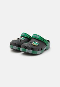 Black clogs with green accents and contrasting gray striped sole. Features decorative pins on the upper and ventilation holes throughout.