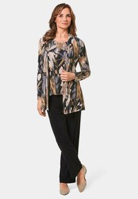 Langsleeve bloemen top in zwart, beige en grijs, gecombineerd met zwarte broek en beige hakken. Zacht, vallend materiaal met een ontspannen silhouet.