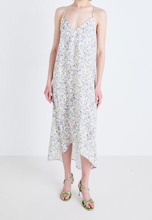 Ärmelloses Midikleid in blassem Gelb mit blauem Blumenmuster, V-Ausschnitt, fließendem Stoff und hohem-niedrigem Saum. Kombiniert mit grünen Riemchen-Absätzen.