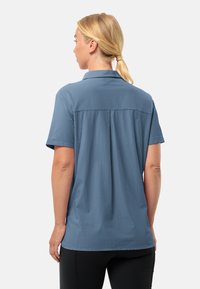 Short-sleeve, collared shirt in light blue fabric with a textured pattern, featuring a back pleat and a relaxed fit.