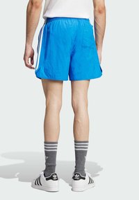 Calções azuis com uma cintura elástica, bolsos laterais e riscas brancas laterais. Combinados com meias grisalhas com riscas e ténis brancos.