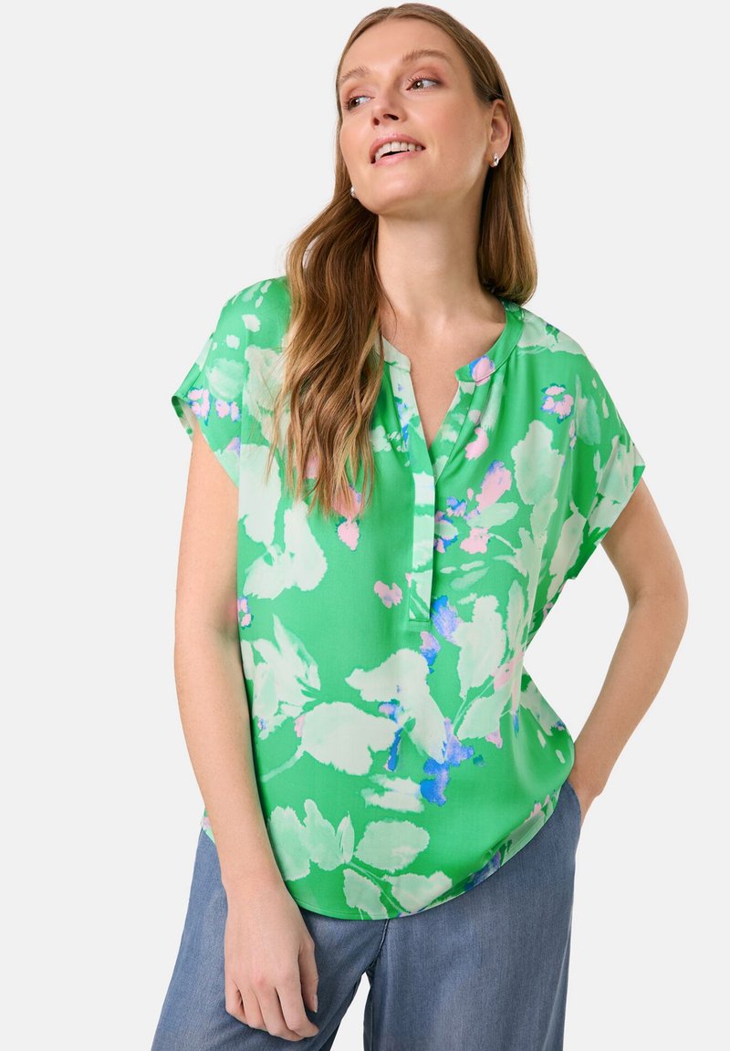 Grüne kurzärmelige Bluse mit floralem Druck in Hellrosa und Blau. Knopfkragen und glattes, leichtes Material. Abgerundeter Saum.