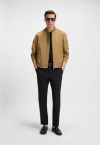 Beezh bomberjakk luku eesliistu ja soonikkoes mansettidega, kantud musta polosärgiga, ühendatud mustade pükste ja susskingadega.