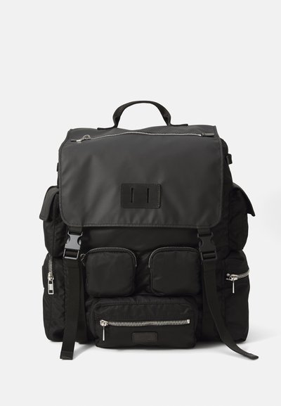 Rucsac negru din nylon, dotat cu închidere cu clapetă, mai multe buzunare cu fermoar, bretele ajustabile și un mâner superior pentru opțiuni de transport.