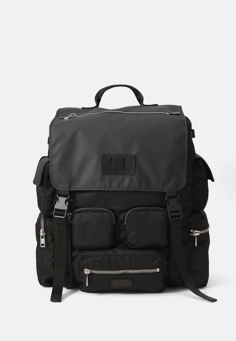 Fekete nylon hátizsák, fedélzáras kivitelezéssel, több cipzáras zsebbel, állítható pántokkal és kézre fogható fogantyúval, amely többféle hordozási lehetőséget kínál.