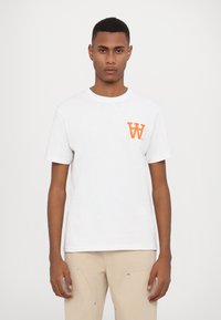 Hvit bomull T-skjorte med en liten oransje "W" logo på venstre bryst. Korte ermer og rund hals. Glatt tekstur.