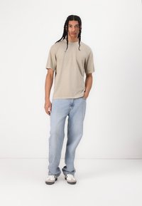 Beige kortærmet skjorte med en afslappet pasform, parret med lyseblå lige ben jeans. Sneakers har et sort og hvidt design.
