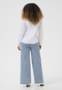 White top with lace long sleeves, paired with wide-leg light denim jeans. The model wears beige high-heeled shoes.