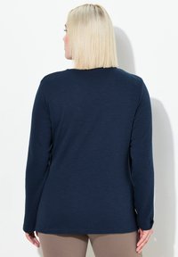 Marineblaues Langarmoberteil aus weichem Material, mit lässigem Schnitt und rundem Ausschnitt. Glatte Textur ohne sichtbare Muster oder Akzente.