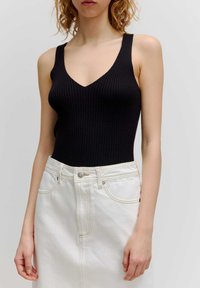 Schwarzer gerippter Body mit tiefem V-Ausschnitt und breiten Trägern, kombiniert mit einem hochtaillierten weißen Denimrock mit sichtbaren Nähten und einem Knopf.