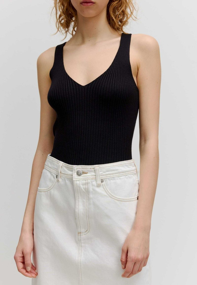 Schwarzer gerippter Body mit tiefem V-Ausschnitt und breiten Trägern, kombiniert mit einem hochtaillierten weißen Denimrock mit sichtbaren Nähten und einem Knopf.