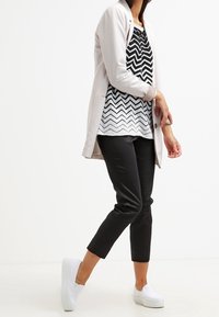 Blazer beige clair sur un haut à motifs zigzag noir et blanc, associé à un pantalon noir fuselé et des baskets blanches.