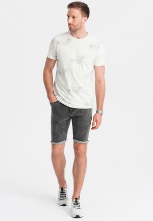 T-shirt blanche avec un motif tacheté subtil, associée à un short en denim gris foncé roulé et des baskets blanches avec des accents noirs.