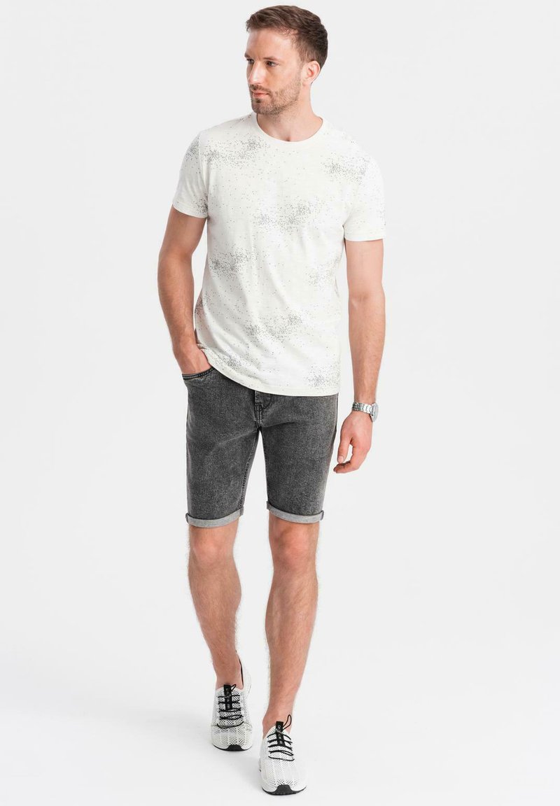 Camiseta blanca con un sutil patrón moteado, combinada con pantalones cortos de mezclilla oscuros y enrollados, y zapatillas blancas con detalles en negro.