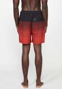 Costume da bagno con gradiente nero e rosso, dotato di vita elastica, strisce orizzontali e un design della tasca a contrasto.