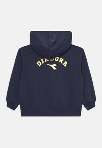 Tumši zilas krāsas kapuce ar priekšējo kenguru kabatu, pievilkšanas kapuci un dzelteno "DIADORA" logo arka formā aizmugurē. Mīksta, teksturēta auduma.