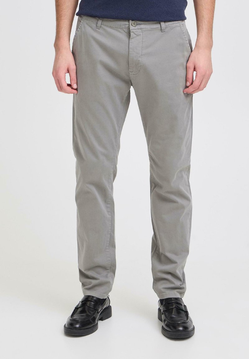 Pantalon en coton gris à coupe slim, avec quatre poches et une texture lisse. Porté avec des chaussures noires ornées d'une boucle.