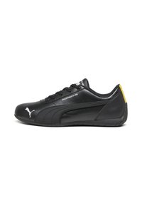 Chaussures Puma noires avec tige en cuir, bout rond et design élégant. Présentent un logo blanc, un accent jaune au talon et une semelle en caoutchouc texturée.