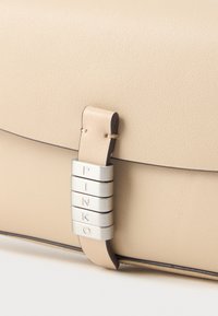 Beżowa skórzana torebka o gładkiej teksturze, z srebrnymi akcentami i owiniętym uchwytem, z widoczną nazwą marki "PINKO."