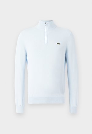 Svetlo modrý pletený sveter s dlhým rukávom a golierom na štvrť-zips s malým zeleným logom krokodíla na pravej hrudi.