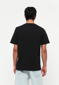 Camiseta negra de manga corta, hecha de algodón, con cuello redondo y corte recto, combinada con jeans de mezclilla azul claro.