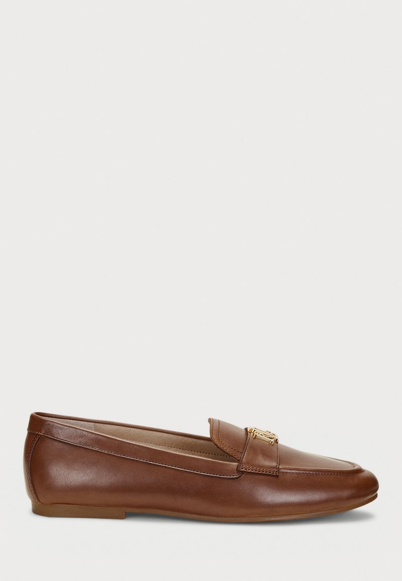 Mocassins de couro castanho com sola plana, apresentando um design costurado e um detalhe em hardware dourado. Textura suave e biqueira arredondada.