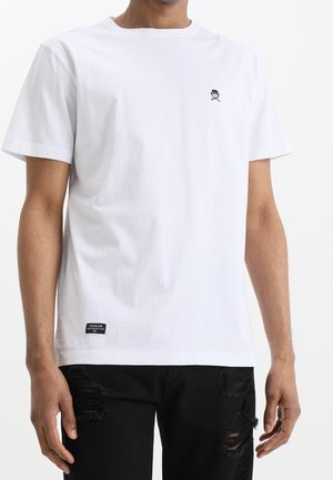 White cotton t-shirt with a round neck, featuring a small black skull and crossbones logo on the chest and a black brand tag at the bottom.