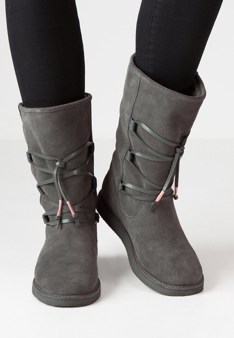 Bottines en suède gris à tige haute, avec des lacets décoratifs et des accents roses. Texture lisse et semelle plate en caoutchouc.